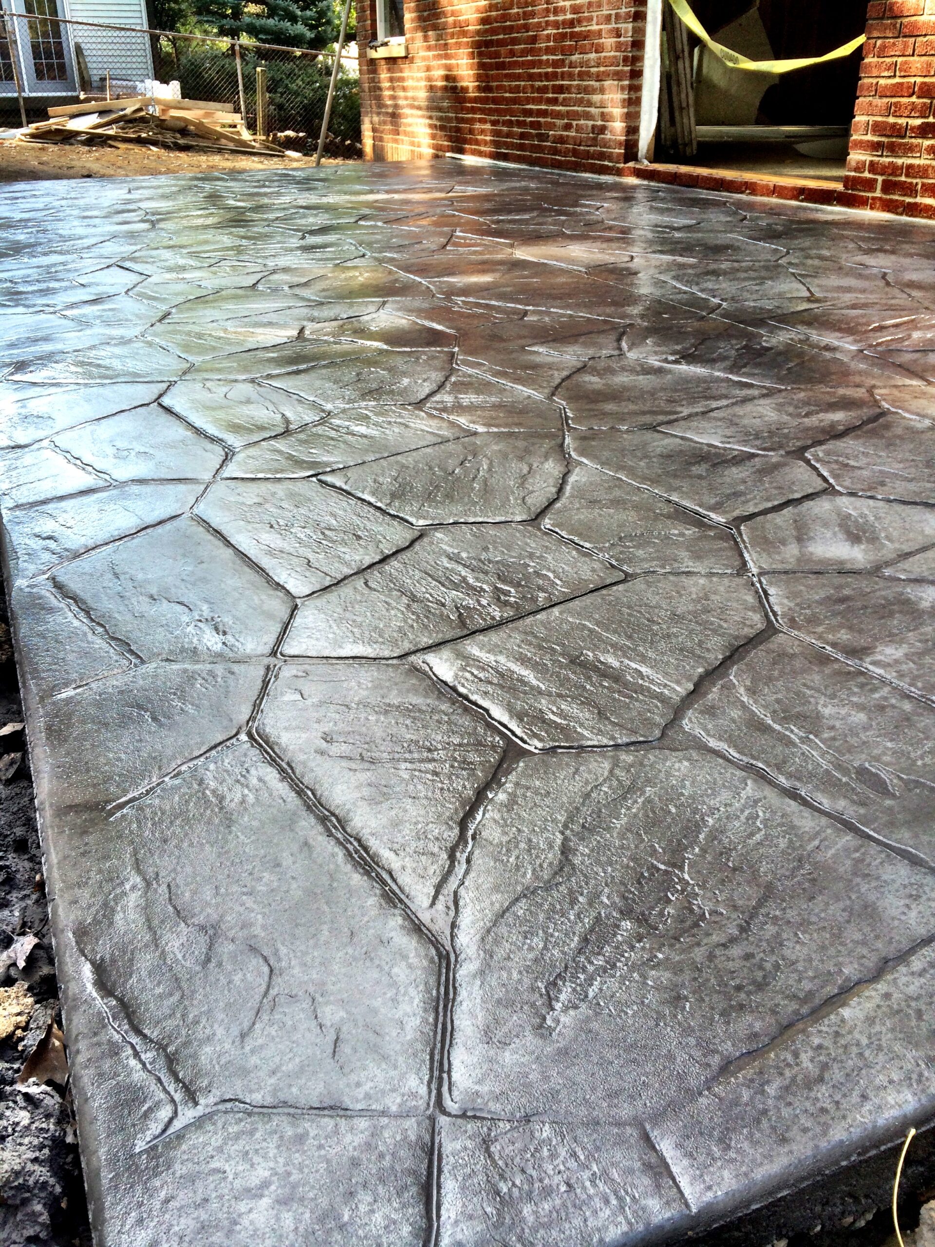 A stamped concrete patio with a stone pattern is shown next to a brick house.