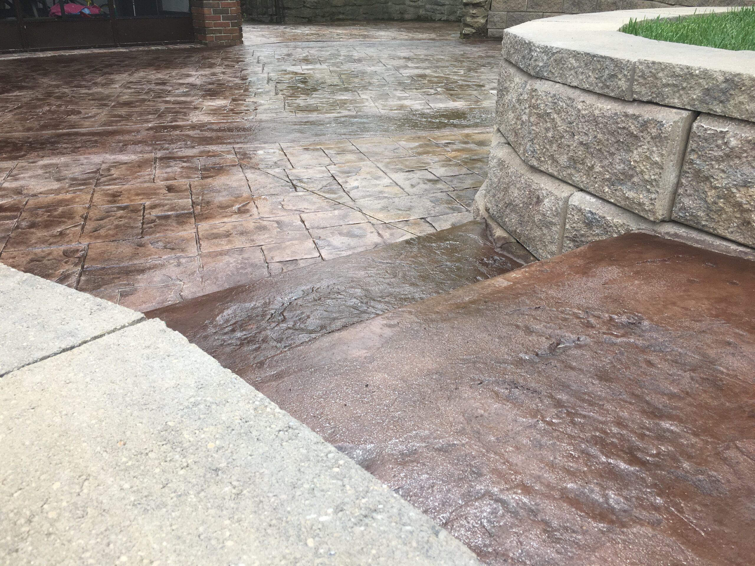 A shallow concrete ramp with a stamped pattern leads up beside a stone retaining wall and a level patio area.